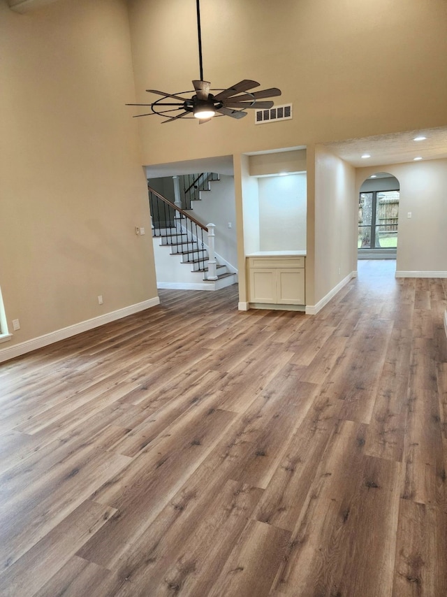 unfurnished living room with arched walkways, visible vents, wood finished floors, baseboards, and stairs