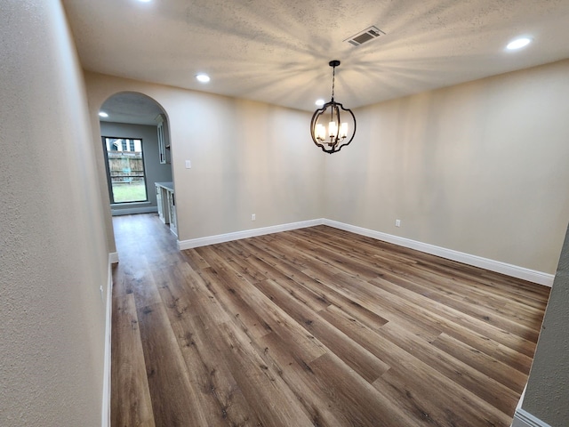 spare room with arched walkways, visible vents, a textured ceiling, wood finished floors, and baseboards