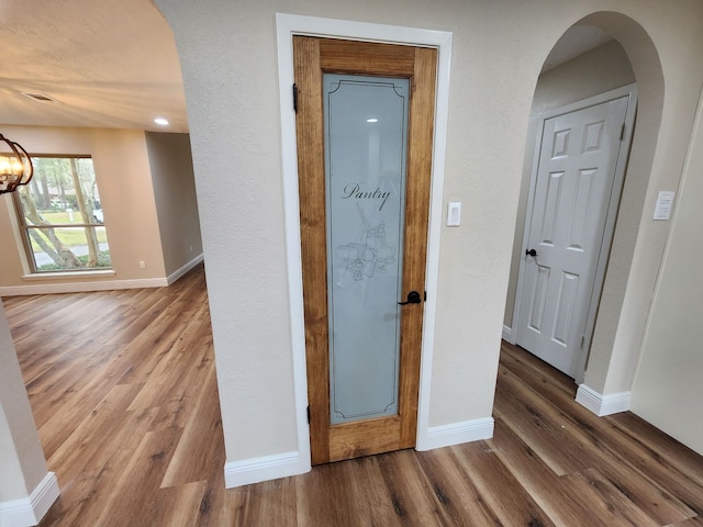 corridor featuring arched walkways, wood finished floors, and baseboards