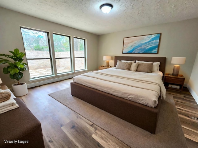 bedroom featuring a textured ceiling, baseboards, and wood finished floors