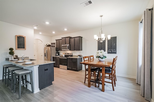 kitchen with arched walkways, stainless steel appliances, visible vents, hanging light fixtures, and light wood-type flooring