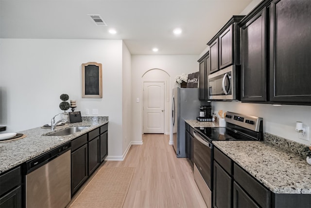 kitchen with appliances with stainless steel finishes, light wood-type flooring, a sink, and light stone counters