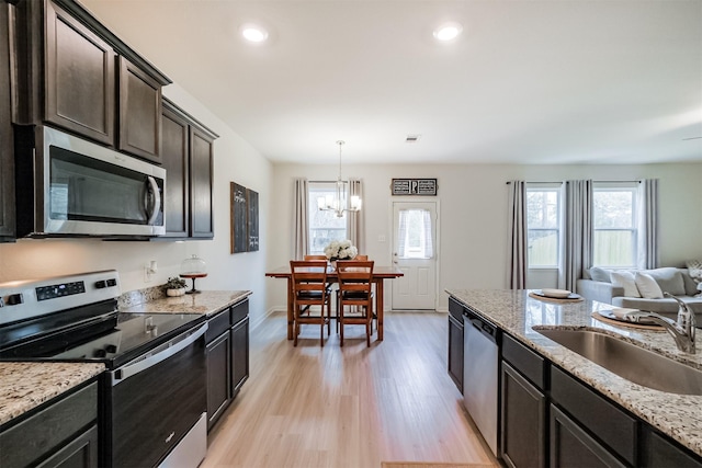 kitchen with light wood finished floors, appliances with stainless steel finishes, light stone counters, decorative light fixtures, and a sink