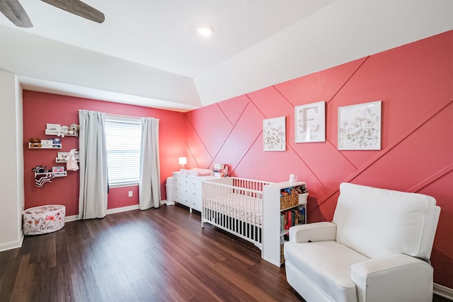 bedroom with a crib, ceiling fan, baseboards, and dark wood-style flooring