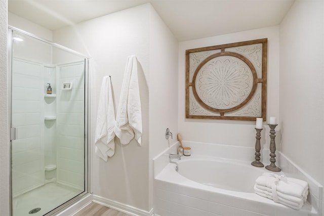 full bathroom featuring a stall shower, a garden tub, and wood finished floors