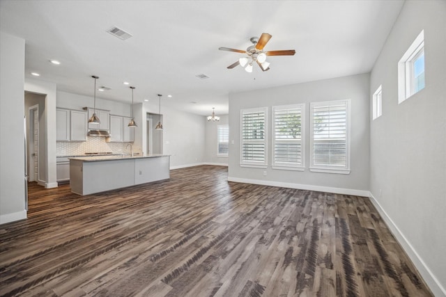 unfurnished living room featuring visible vents, baseboards, dark wood-style flooring, and ceiling fan with notable chandelier