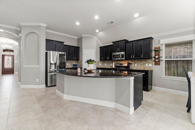 kitchen with an island with sink, appliances with stainless steel finishes, dark stone counters, and dark cabinetry