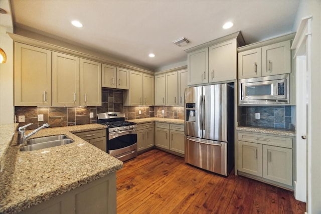 kitchen featuring stainless steel appliances, sink, backsplash, light stone counters, and dark hardwood / wood-style floors