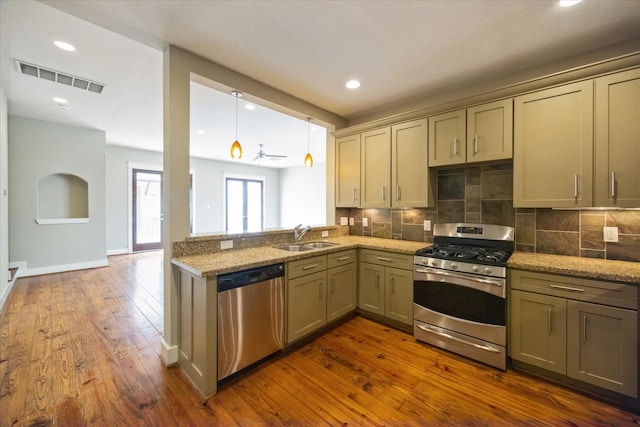 kitchen with hardwood / wood-style floors, sink, pendant lighting, stainless steel appliances, and light stone countertops