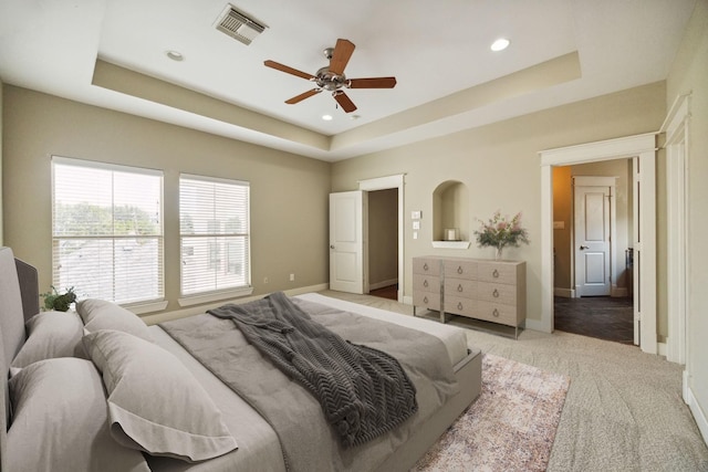 bedroom with light carpet, ceiling fan, and a tray ceiling