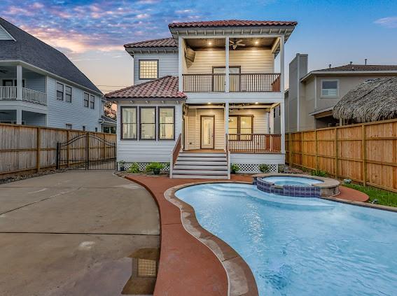 back house at dusk with a swimming pool with hot tub, a balcony, ceiling fan, and a patio area