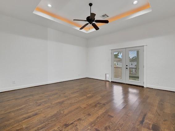 empty room featuring ceiling fan, french doors, dark hardwood / wood-style flooring, and a raised ceiling