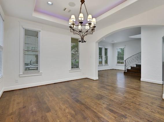 unfurnished dining area with a tray ceiling, a chandelier, and dark hardwood / wood-style floors