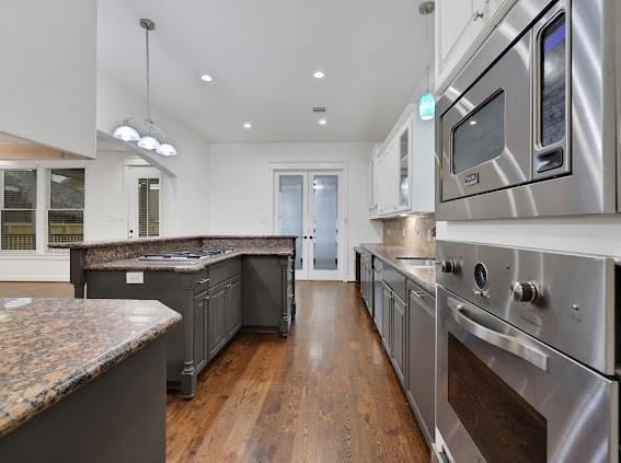 kitchen featuring stainless steel appliances, decorative light fixtures, a kitchen island, dark stone counters, and white cabinets