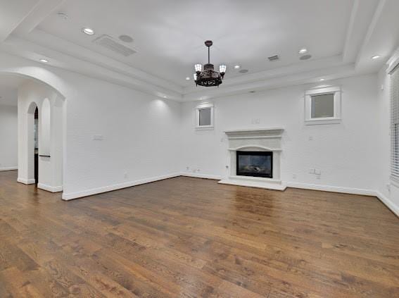 unfurnished living room with dark hardwood / wood-style flooring, a raised ceiling, and an inviting chandelier