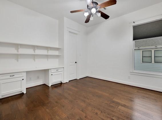 unfurnished office featuring ceiling fan, built in desk, and dark wood-type flooring