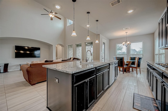 kitchen featuring an island with sink, sink, light stone counters, appliances with stainless steel finishes, and pendant lighting