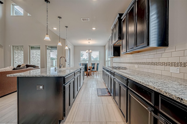 kitchen with decorative light fixtures, sink, an island with sink, and light stone countertops