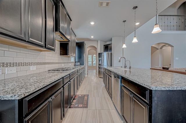 kitchen with appliances with stainless steel finishes, light stone counters, decorative light fixtures, sink, and a kitchen island with sink