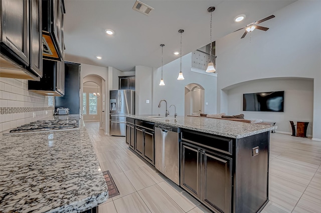 kitchen featuring a center island with sink, hanging light fixtures, stainless steel appliances, light stone countertops, and sink