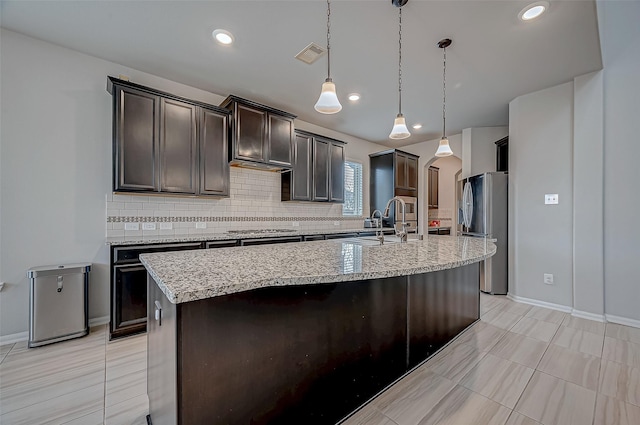 kitchen with a center island with sink, stainless steel appliances, decorative light fixtures, sink, and backsplash