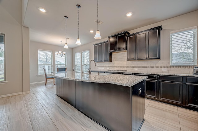 kitchen with a kitchen island with sink, stainless steel gas stovetop, sink, tasteful backsplash, and pendant lighting