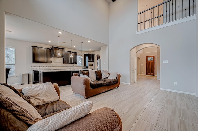 tiled living room featuring wine cooler, sink, and a high ceiling