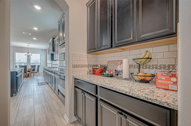 kitchen featuring an inviting chandelier, backsplash, oven, decorative light fixtures, and light stone countertops