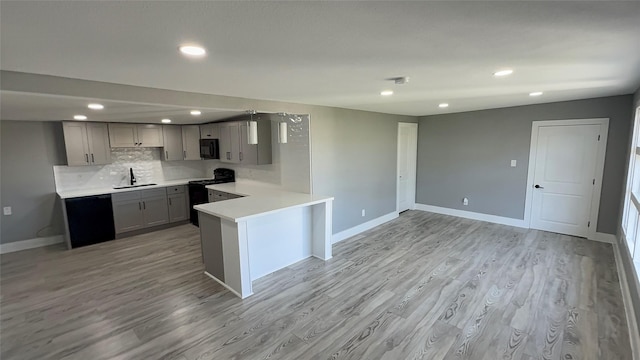 kitchen featuring kitchen peninsula, gray cabinetry, light hardwood / wood-style flooring, black appliances, and tasteful backsplash