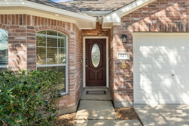 property entrance with a garage, a shingled roof, and brick siding