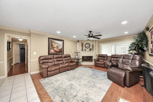 living area with crown molding, a fireplace, visible vents, light wood-style flooring, and ceiling fan