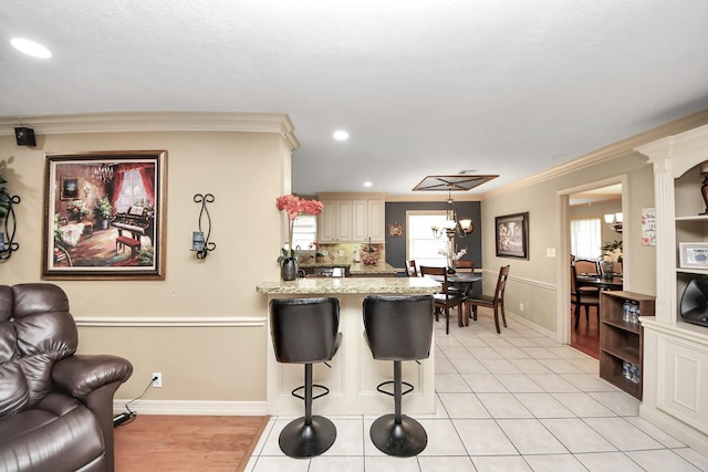 kitchen featuring a notable chandelier, crown molding, a breakfast bar area, a peninsula, and baseboards