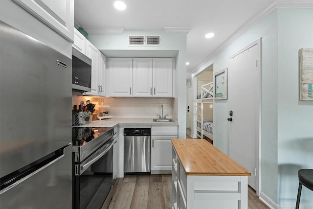 kitchen with crown molding, stainless steel appliances, visible vents, a sink, and butcher block countertops