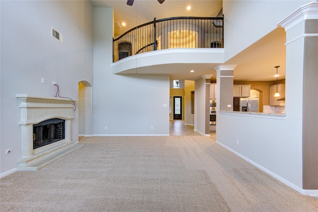 unfurnished living room with light colored carpet, baseboards, visible vents, a fireplace with raised hearth, and a ceiling fan