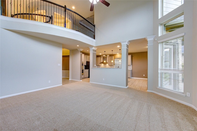 unfurnished living room featuring ornate columns, light colored carpet, a ceiling fan, and baseboards