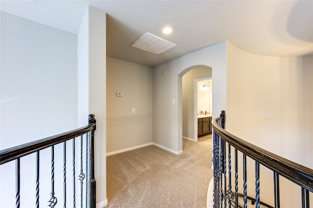 hallway featuring an upstairs landing, light colored carpet, baseboards, arched walkways, and a sink