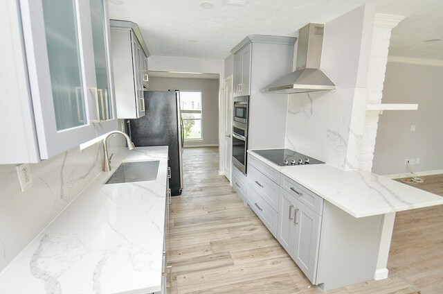 kitchen featuring gray cabinetry, wall chimney range hood, light wood-type flooring, stainless steel appliances, and a sink