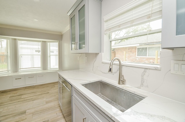 kitchen featuring tasteful backsplash, crown molding, dishwasher, light wood-style flooring, and a sink