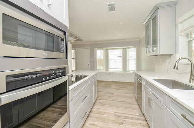 kitchen featuring visible vents, light wood-style flooring, a sink, stainless steel appliances, and crown molding