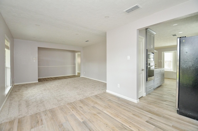 unfurnished room featuring light colored carpet, light wood-style floors, visible vents, and baseboards