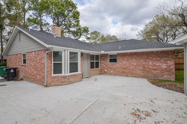 rear view of property featuring brick siding, fence, roof with shingles, a chimney, and a patio area