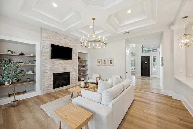 living area with built in shelves, light wood-style flooring, a stone fireplace, a chandelier, and baseboards