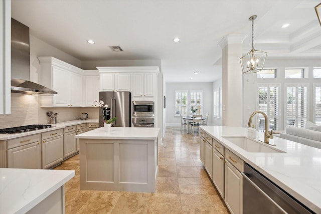 kitchen featuring a center island, visible vents, appliances with stainless steel finishes, a sink, and wall chimney range hood