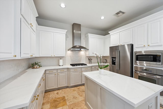 kitchen with visible vents, wall chimney exhaust hood, a kitchen island, appliances with stainless steel finishes, and white cabinetry