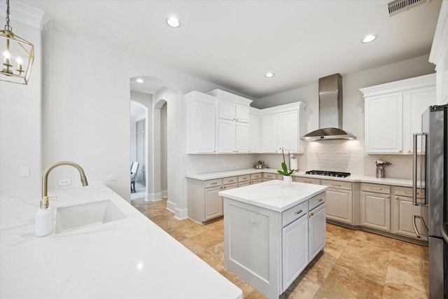 kitchen with wall chimney exhaust hood, hanging light fixtures, a sink, and white cabinets