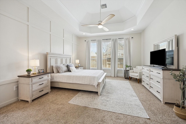 bedroom with a tray ceiling, visible vents, a decorative wall, ornamental molding, and light carpet