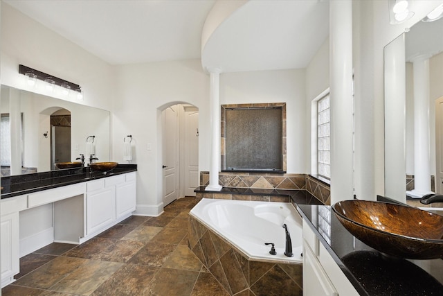 bathroom featuring stone finish flooring, a garden tub, vanity, and decorative columns