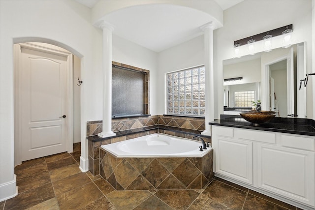 full bathroom with decorative columns, vanity, stone tile floors, and a bath