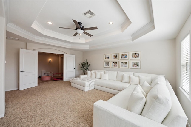 carpeted living room featuring ornamental molding, a tray ceiling, visible vents, and a ceiling fan