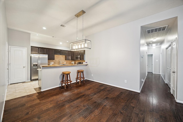 kitchen featuring visible vents, appliances with stainless steel finishes, wood finished floors, a peninsula, and dark brown cabinets